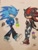 Size: 4032x3024 | Tagged: safe, artist:jaidenlovestodraw, shadow the hedgehog, sonic the hedgehog, 2023, alternate universe, clothes, crop top, duo, ear piercing, earring, fingerless gloves, hands in pocket, jacket, jeans, lidded eyes, lollipop, looking offscreen, mouth hold, pansexual, pansexual pride, pants, ripped pants, shirt, standing, traditional media, trainers, trans male, trans pride, transgender, transmasculine, walking